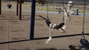 Happy adult skeleton side view swinging slow motion in empty closed park 