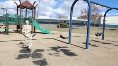 Happy adult skeleton side view swinging playing in empty park