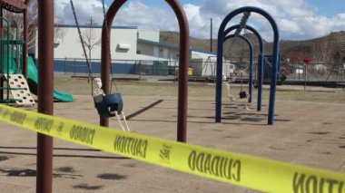 Side view child and adult skeletons swinging wearing face masks at closed play area due to virus