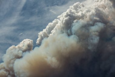 Mavi ve beyaz gökyüzü kabarık kümülonimbus bulutları ve büyük bir yangından çıkan duman