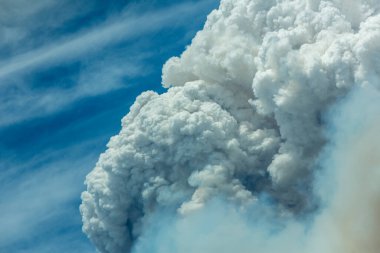 Mavi ve beyaz gökyüzü kabarık kümülonimbus bulutları ve büyük bir yangından çıkan duman