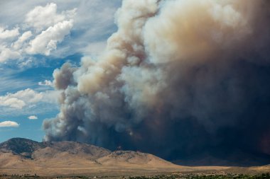 Mavi ve beyaz gökyüzü kabarık kümülonimbus bulutları ve çöldeki büyük bir yangından çıkan duman.