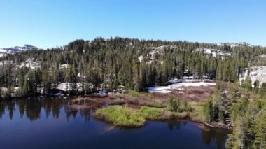 Drone pan left over lake mountains trees and snow patches in the winter