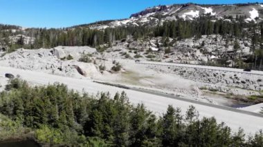 Drone pan right over trees mountains rocks with snow freeway traffic.