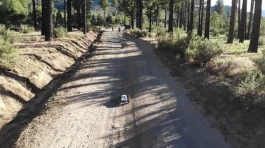 İnsansız hava aracı ağır çekimde toprak yolda insanlara doğru gidiyor.