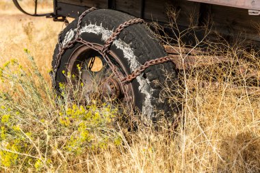 Çimenli bir tarlada, yıpranmış bir lastiğin metal kar zincirleri.