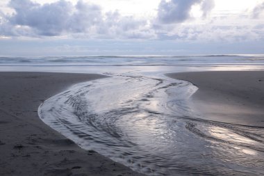 Yokuş yukarı okyanusa akan dere suyu gün batımından sonra bulutların güzel yansımaları.