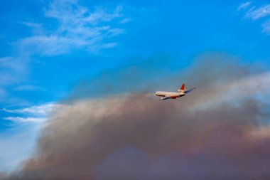 Yoğun karanlık yangın dumanının içinden uçan yangın uçağı geciktirici bırakıyor.