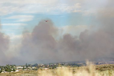 İtfaiye helikopteri, büyük ateş bulutlarının üzerinde bir su kovası taşıyor.