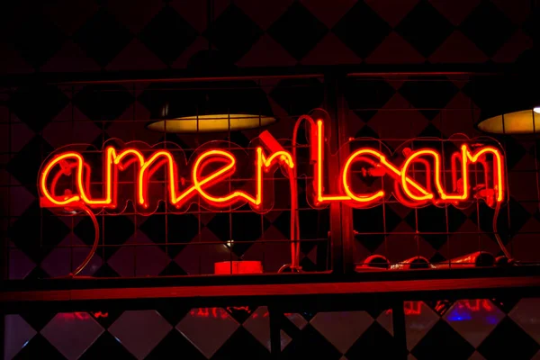 Glowing Neon red sign AMERICAN and blurred lights on black background.