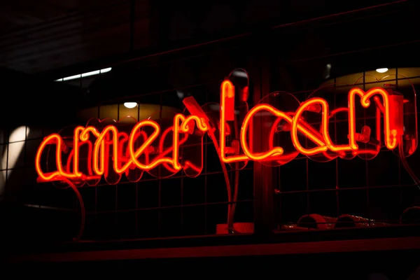 Glowing Neon red sign AMERICAN and blurred lights on black background.