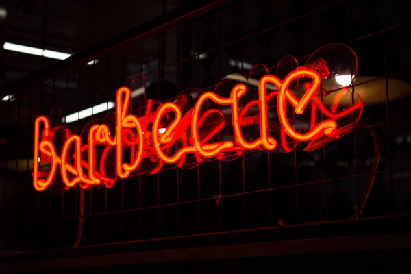 Glowing Neon red sign BARBECUE and blurred lights on black background.