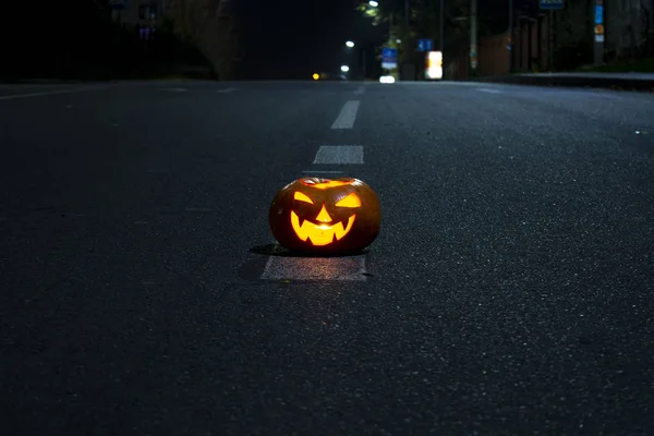 Halloween pumpkin with carved demonic face and candles inside on the night road. — Stock Photo, Image