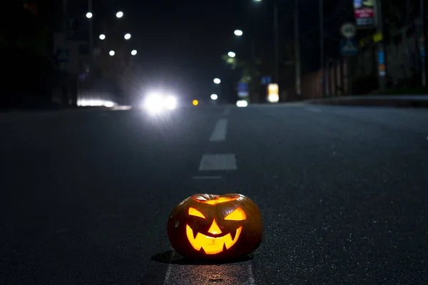Halloween pumpkin with carved demonic face and candles inside on the night road.