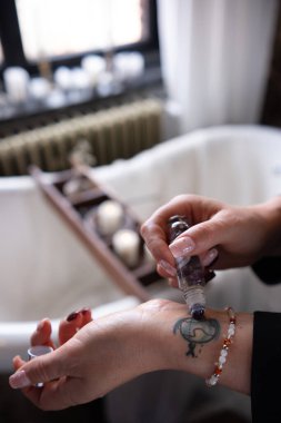 Bir kadın aroma silindiri kullanarak bileğine aroma yağı sürer. Bileğinde çok güzel bir dövme, arka planda bir küvet ve mumlar var..