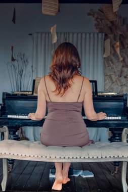 Klasik piyanonun yanında müzik kağıtlarıyla poz veren güzel bir kadın. Güzel elbiseli bir kız antika iç mekan, klasik piyano ve aksesuarlarla poz veriyor..