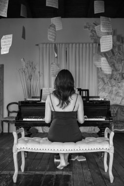 Klasik piyanonun yanında müzik kağıtlarıyla poz veren güzel bir kadın. Güzel elbiseli bir kız antika iç mekan, klasik piyano ve aksesuarlarla poz veriyor..