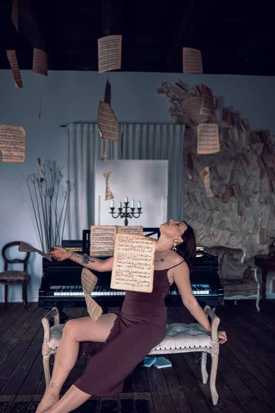 Klasik piyanonun yanında müzik kağıtlarıyla poz veren güzel bir kadın. Güzel elbiseli bir kız antika iç mekan, klasik piyano ve aksesuarlarla poz veriyor..