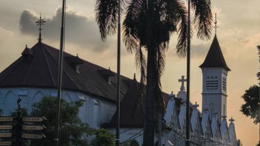 Bogor, Endonezya - 3 Eylül 2025: Tropikal palmiye ağaçları ile güzel bir günbatımı gökyüzüne karşı siluetlenmiş tarihi kiliseler ve çan kulesi.