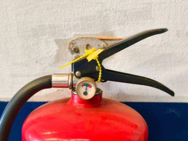 Parlak kırmızı yangın söndürme tüpü, sapı, hortumu ve basınç göstergesi, sarı bir kravat ile korunuyor, yangın korumaya ve arka planda acil durum kullanımına hazır..