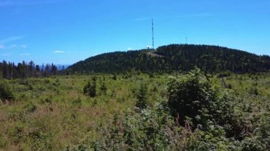 Telekomünikasyon anten kulesi açık mavi bir gökyüzünün altındaki yeşil bir dağın tepesinde duruyor..