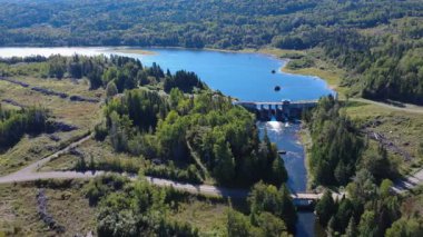 Mitis Gölü 'nün su seviyesini kontrol eden eski Mitis Barajı' nın panoramik hava manzarası. Orman, odun yığınları ve odunluk yollarıyla çevrili. Quebec, Kanada, 2025.