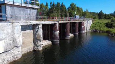 Yaşamının sonuna yaklaşan eski bir baraj, yaya köprüsünün altındaki çökmekte olan beton sütunları güçlendirmek için inşa edilmiş eğri çelik plakalarını ortaya çıkarıyor. Mitis Barajı, Quebec, Kanada, 2025.