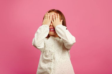 Küçük kız elleriniz ve izole pembe gülümsüyor gözleri kapalı.