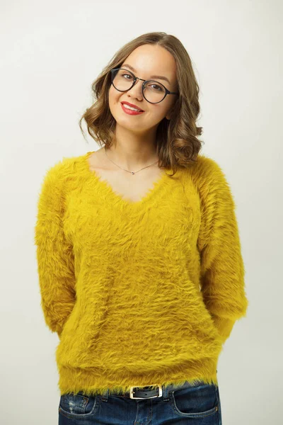 Retrato de menina bonita em suéter amarelo brilhante, usa óculos redondos, tem uma expressão agradável, olhar sincero e sorriso encantador, de pé sobre branco isolado . — Fotografia de Stock