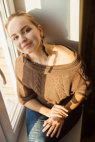 Beautiful sensual woman with earrings sitting on window looks camera