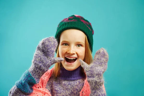 Portrét dívky, veselé dítě nosí zimní palčáky, Teplý svetr, čepice s bambulí a prolamované mys šátek na modrém pozadí izolované. — Stock fotografie