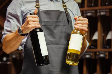 Genç sommelier şişe kırmızı şarap mahzeninde tutuyor