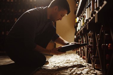 Şişelerden birine ahşap bodrumdan alarak sommelier