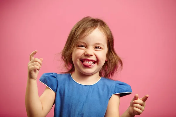 Портрет радісної маленької дівчинки в гарному гуморі, кусає язик, піднімає руки вгору . — стокове фото