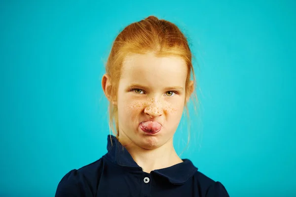 Traviesa pelirroja chica muestra la lengua y se burla de usted, primer plano retrato en azul aislado fondo . — Foto de Stock