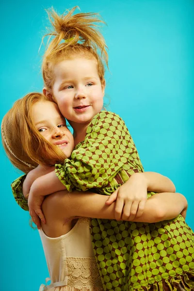 Two little red headed girls sisters hug each other warmly, express sincere relationship of love and care.