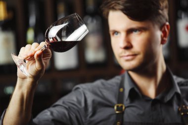 Arka planda bir şişe kırmızı şarap, erkek şarap garsonu içkinin değerini biliyor.