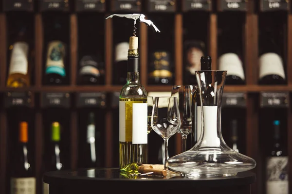 Bottle of white wine on the table next to decanter and glasses over shelf background. — Stock Photo, Image