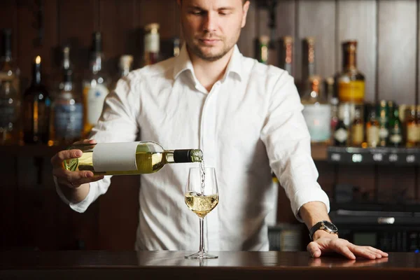 Sommelier in shirt pouring white wine into glass