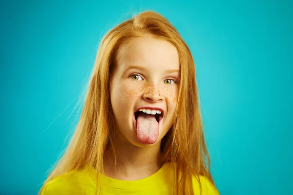 Foto horizontal de niña con ojos expresivos y ojos grandes sacó la lengua, boca abierta, muestra una naturaleza traviesa. Niño mimado en azul aislado . — Foto de Stock