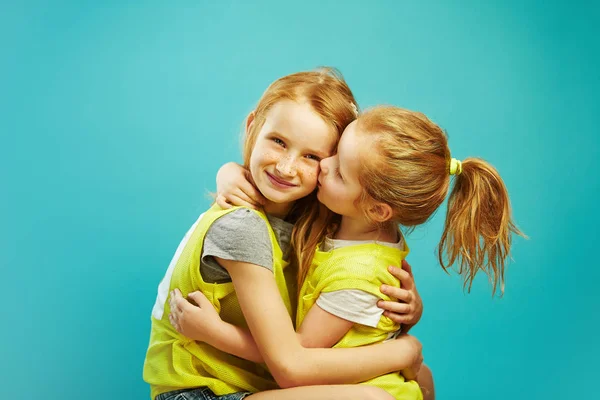 Маленькая девочка целует свою старшую сестру на синем фоне . — стоковое фото