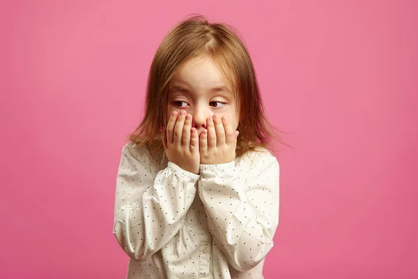 Criança menina cobriu a boca com as mãos e olha para longe com pesar — Fotografia de Stock