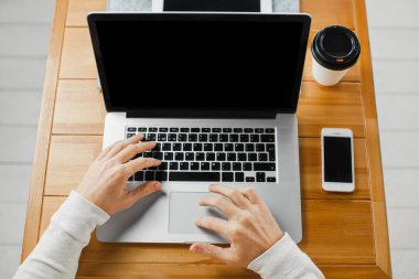 Adam masada dizüstü bilgisayarda yazarak. Fincan kahve ve smartphone