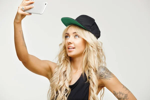 young blond woman makes selfie on front camera of smartphone over white isolated background.