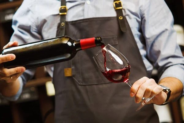 Sommelier masculino derramando vinho tinto em vinhedos de caule longo. — Fotografia de Stock