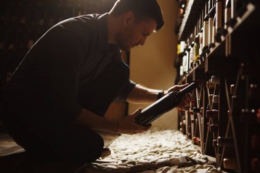 Şişelerden birine ahşap bodrumdan alarak sommelier
