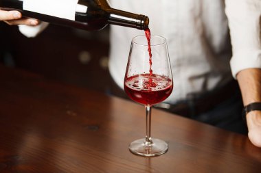Erkek şarap garsonu kırmızı şarabı uzun saplı şarap bardaklarına dolduruyor..