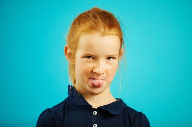 Portrait of redheaded girl showing tongue at the camera over blue background. clipart