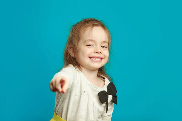 Pequena menina sorridente é aponta o dedo em você sobre fundo isolado azul . — Fotografia de Stock