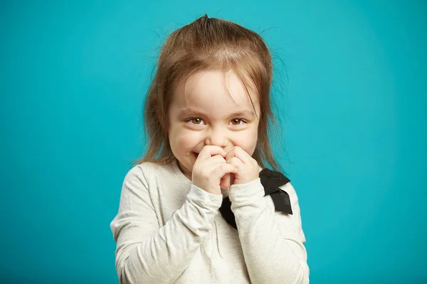 Pequena menina tímida sorri e cobre a boca com as mãos, expressa vergonha e indecisão, foto emocional de crianças timidez no fundo azul . — Fotografia de Stock
